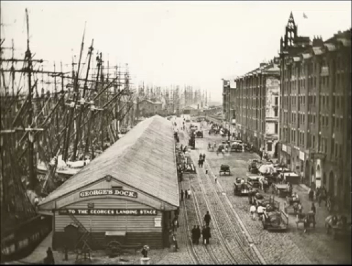 Historical view along George’s Dock toward George’s Landing Stage, with sailing ships, warehouses, carts and pedestrians.